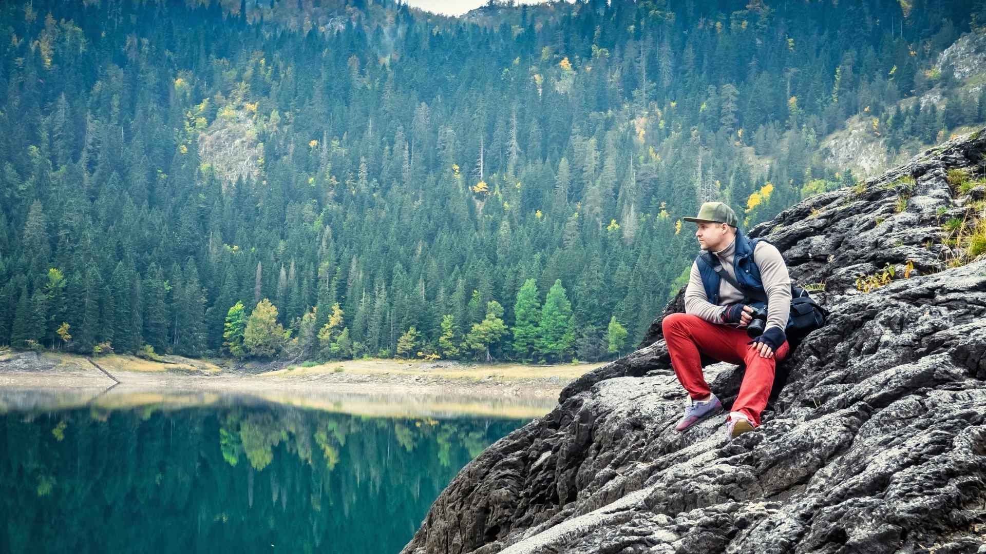 a guy sitting on a hill looking at a lake